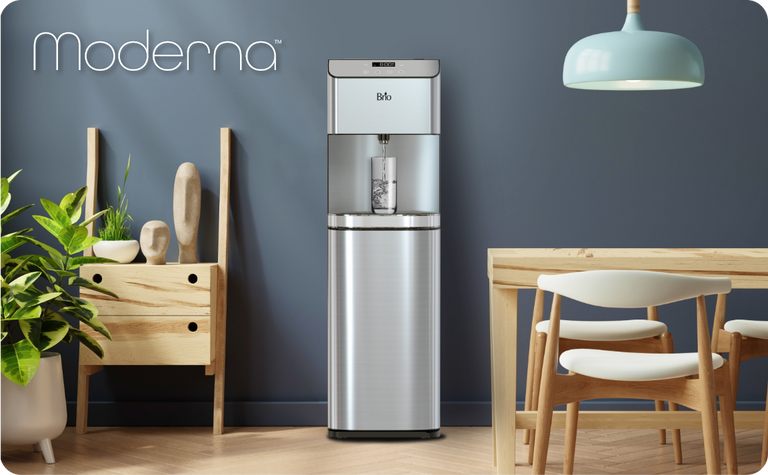 Brio Moderna stainless steel water dispenser in a modern kitchen setting with wooden furniture, indoor plants, and a blue wall.